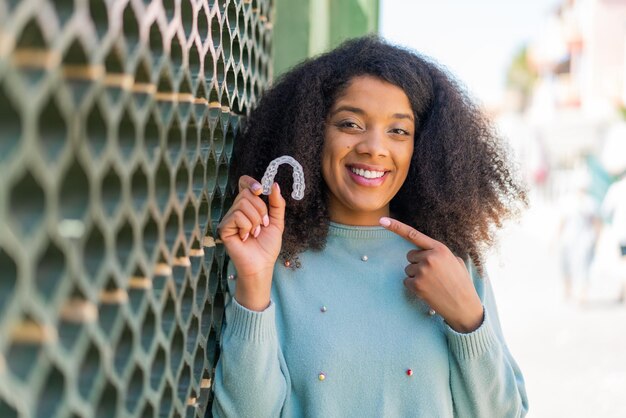 Young African American woman holding invisible braces at outdoors with surprise facial expression