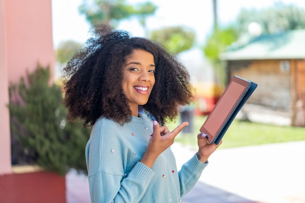 Young African American woman holding a tablet at outdoors and pointing it