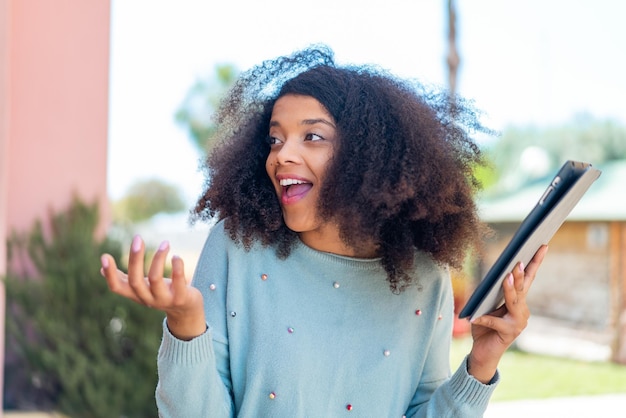 Young African American woman holding a tablet at outdoors with surprise facial expression