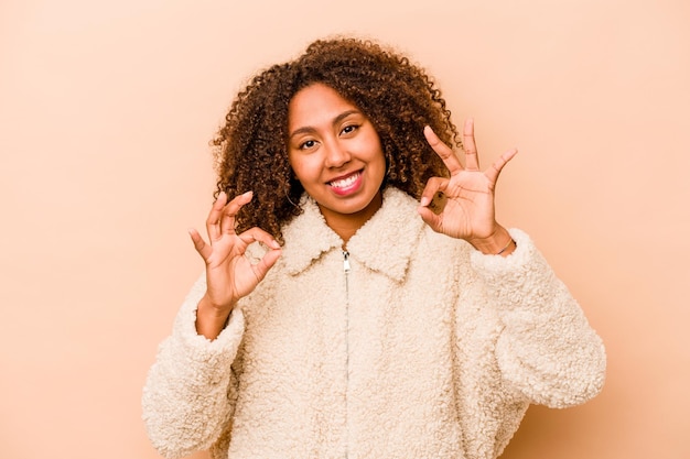 Young African American woman isolated on beige background cheerful and confident showing ok gesture