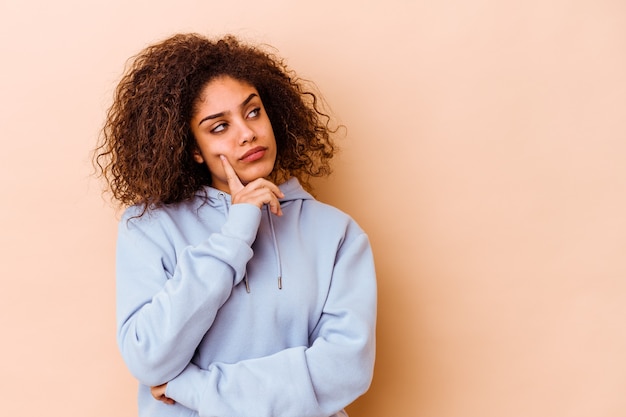 Young african american woman isolated on beige background looking sideways with doubtful and skeptical expression.