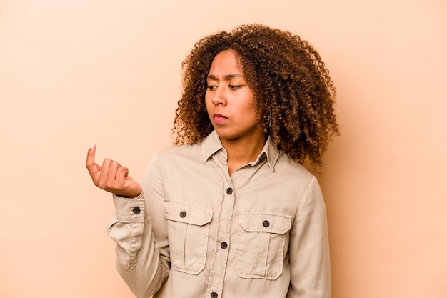 Young African American woman isolated on beige background pointing with finger at you as if inviting come closer