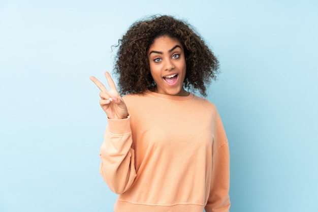 Young African American woman isolated on blue smiling and showing victory sign