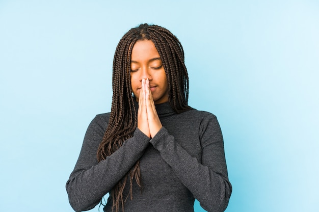 Young african american woman isolated on blue surface holding hands in pray near mouth, feels confident.