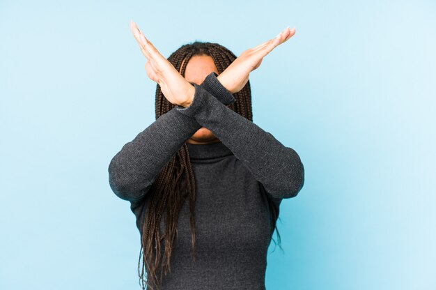 Young african american woman isolated on blue wall keeping two arms crossed, denial concept.