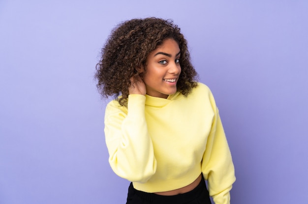 Young African American woman isolated on listening to something by putting hand on the ear