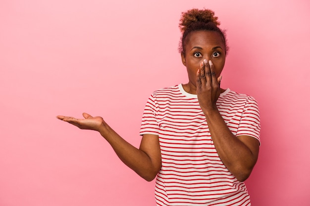 Young african american woman isolated on pink background impressed holding copy space on palm.