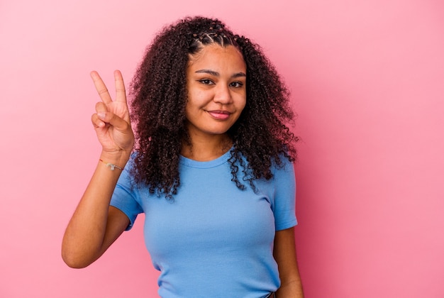 Young african american woman isolated on pink background joyful and carefree showing a peace symbol with fingers.