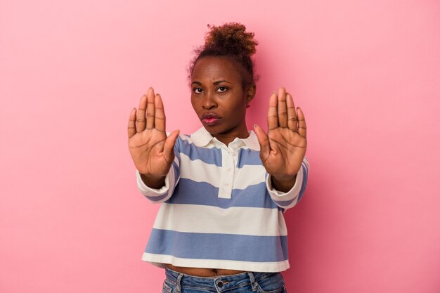 Young african american woman isolated on pink background standing with outstretched hand showing stop sign, preventing you.