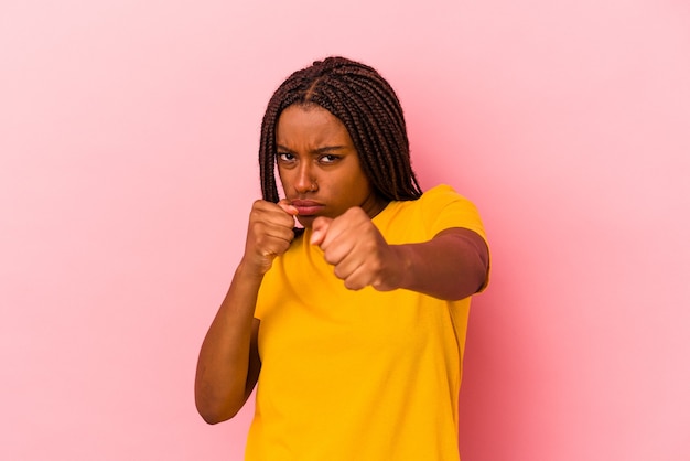 Young african american woman isolated on pink background  throwing a punch, anger, fighting due to an argument, boxing.