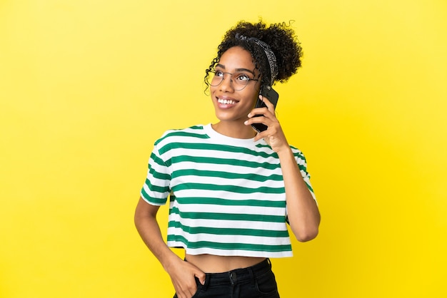 Young african american woman isolated on yellow background keeping a conversation with the mobile phone with someone