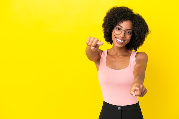 Young African American woman isolated on yellow background pointing front with happy expression