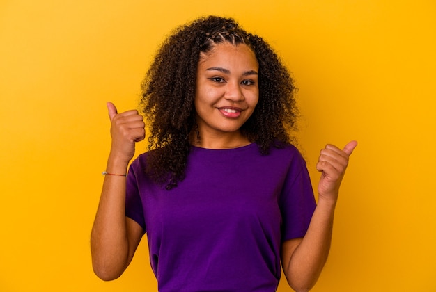 Young african american woman isolated on yellow background raising both thumbs up, smiling and confident.