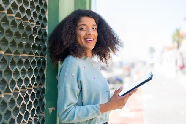 Young African American woman at outdoors holding a tablet with happy expression