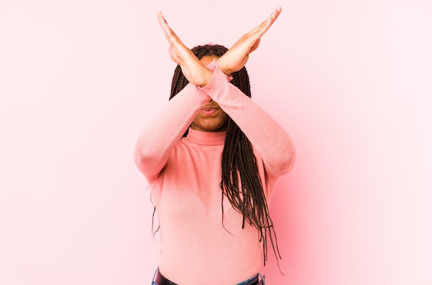 Young african american woman on a pink wall keeping two arms crossed