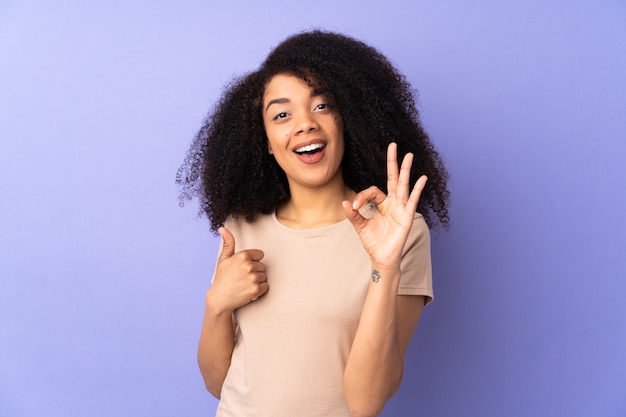 Young african american woman on purple wall showing ok sign and thumb up gesture