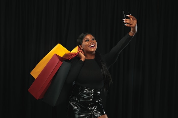 Young african-american woman shopping with colorful packs on black wall.