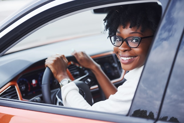 Young african american woman sits inside of new modern car.