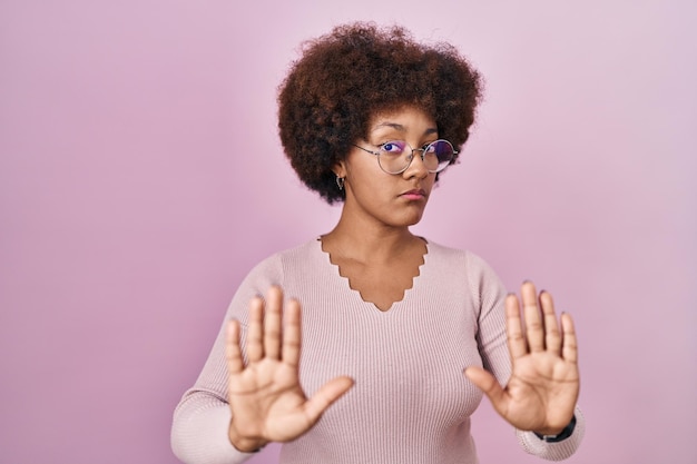 Young african american woman standing over pink background moving away hands palms showing refusal and denial with afraid and disgusting expression. stop and forbidden.