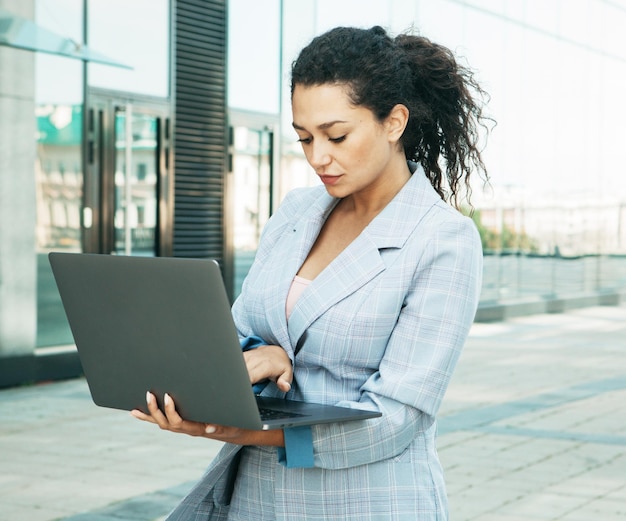 Young african american woman uses laptop outdoors next to business center business concept