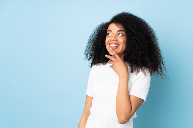 Young african american woman over wall looking up while smiling