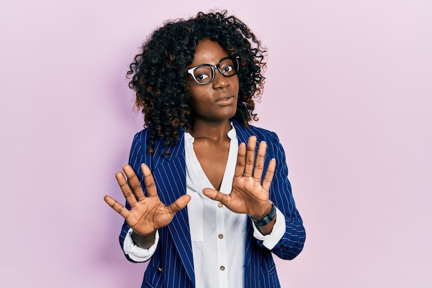 Young african american woman wearing business clothes and glasses moving away hands palms showing refusal and denial with afraid and disgusting expression stop and forbidden