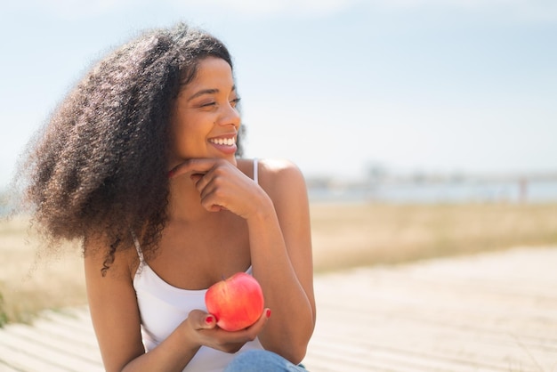 Young African American woman with an apple at outdoors thinking an idea and looking side