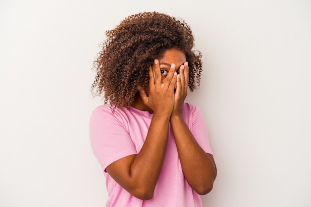 Young african american woman with curly hair isolated on white background blink through fingers frightened and nervous.