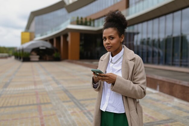 Young african american woman with mobile phone against the background of the facade of an office