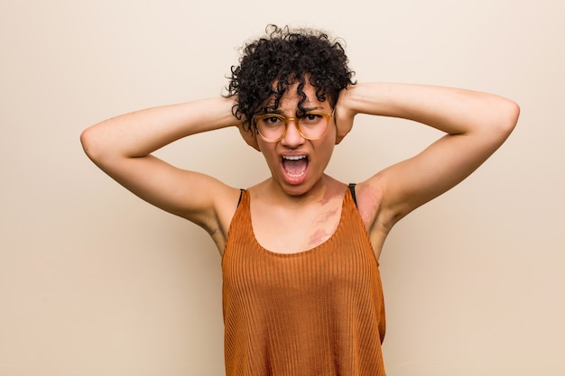 Young african american woman with skin birth mark covering ears with hands trying not to hear too loud sound.