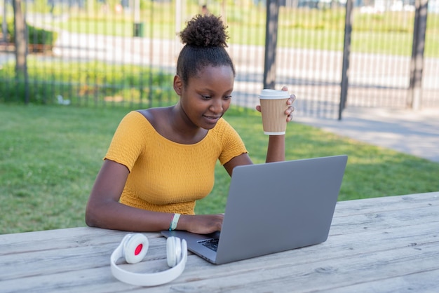 Young african fashion woman studying outdoors blogger working in the city while drinking takeaway coffee i a disposable cup ecologic and sustainability concept