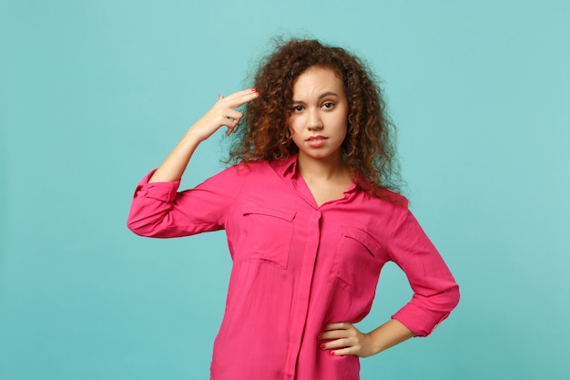 Young african girl in casual clothes point fingers to head as if she about shoot herself isolated on blue turquoise wall background. People sincere emotions, lifestyle concept. Mock up copy space.