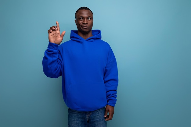 A young african guy in a stylish hoodie demonstrates with his hand on an advertisement on a studio