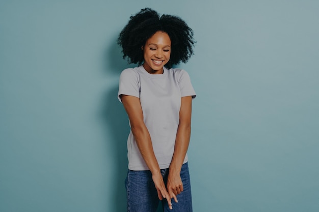 Young african lady looking down with with shy timid face expression isolated over blue background