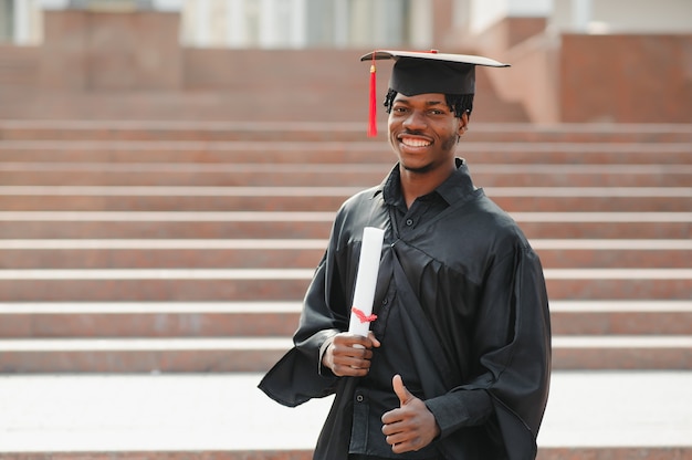 Young african male graduate standing in front of university building