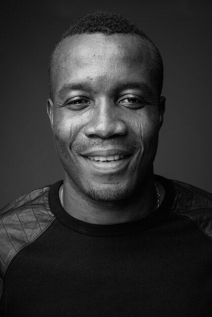 young African man wearing black long sleeved shirt against gray wall. black and white