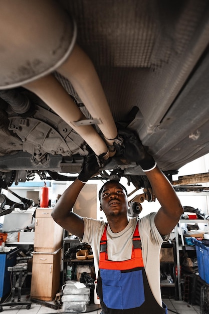 Young african mechanic in uniform working under the car in car service center