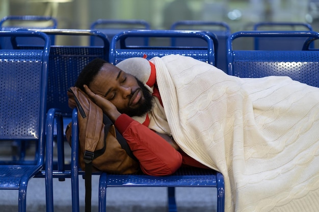 Young african passenger man sleeping under plaid waiting for flight feel cold long night connection