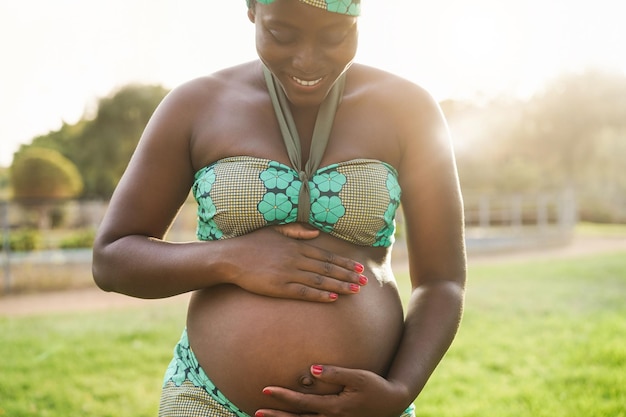 Young african pregnant woman having tender moment touching her belly outdoor at city park  Focus top hand holding belly