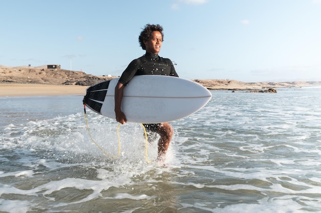 Young african surfer on the beach shore running to the waves