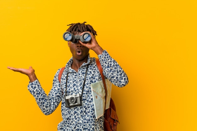 Young african tourist man standing against a yellow background holding a binoculars