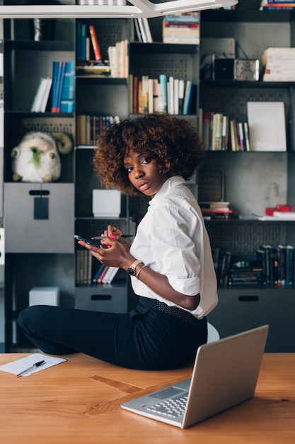 Young african woman posing in modern office with smartphone and looking camera 