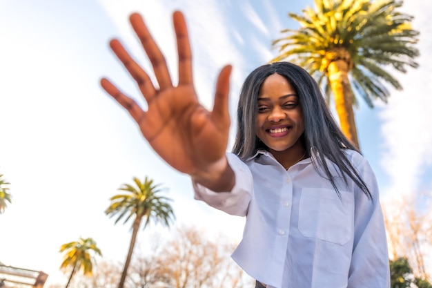 Young african woman posing in white clothes in a tropical place with palm trees at sunset enjoying the summer smiling