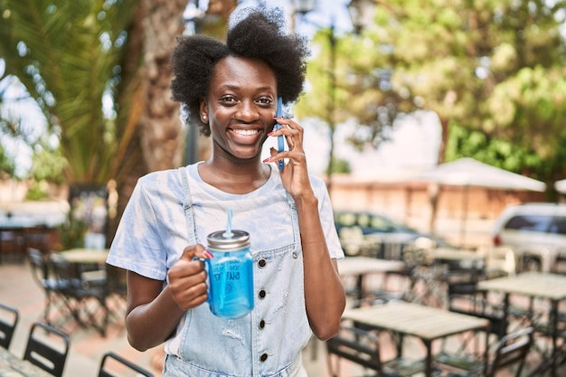 Young african woman talking to the phone holding bottle at street