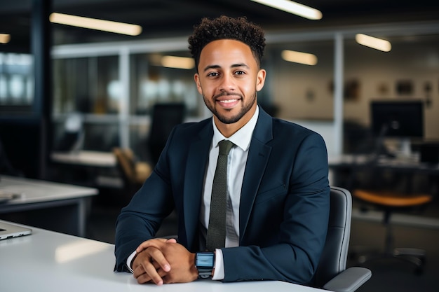 A young AfricanAmerican professional wearing a suit and tie smiles while sitting at his desk in an office