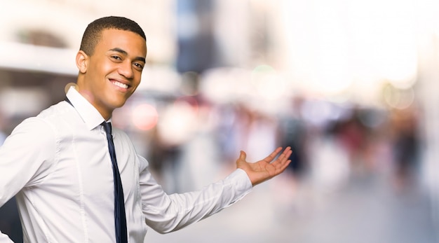 Young afro american businessman pointing back and presenting a product in the city