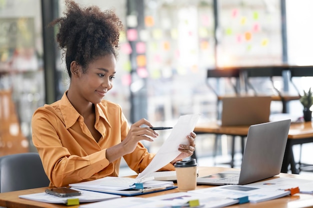 Young afro american businesswoman working on paperwork and laptop computer at open workspace