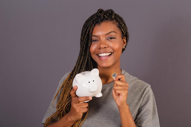 Young afro brazilian woman holding piggy bank and coin concept of economy finance saving