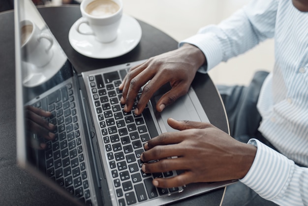 Young afro businessman working on laptop in car showroom. Successful business person on motor show, black man in formal wear