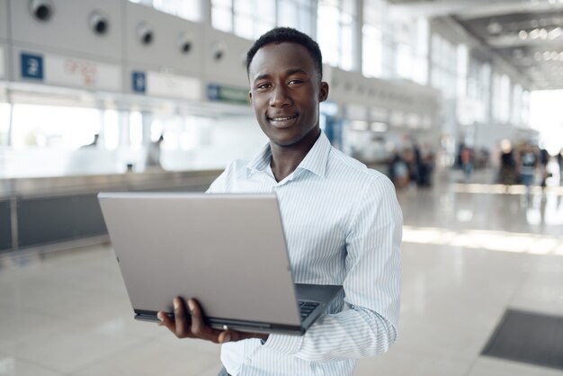 Young afro businessman working on laptop in car showroom. Successful business person on motor show, black man in formal wear